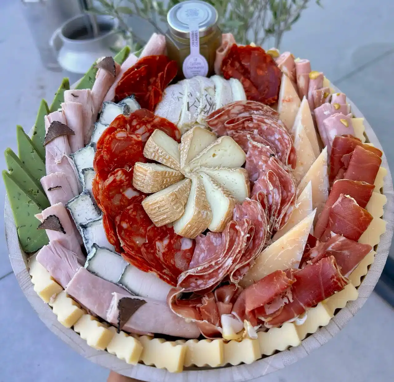 Un plateau rond garni de charcuterie et de fromages disposés en rosace