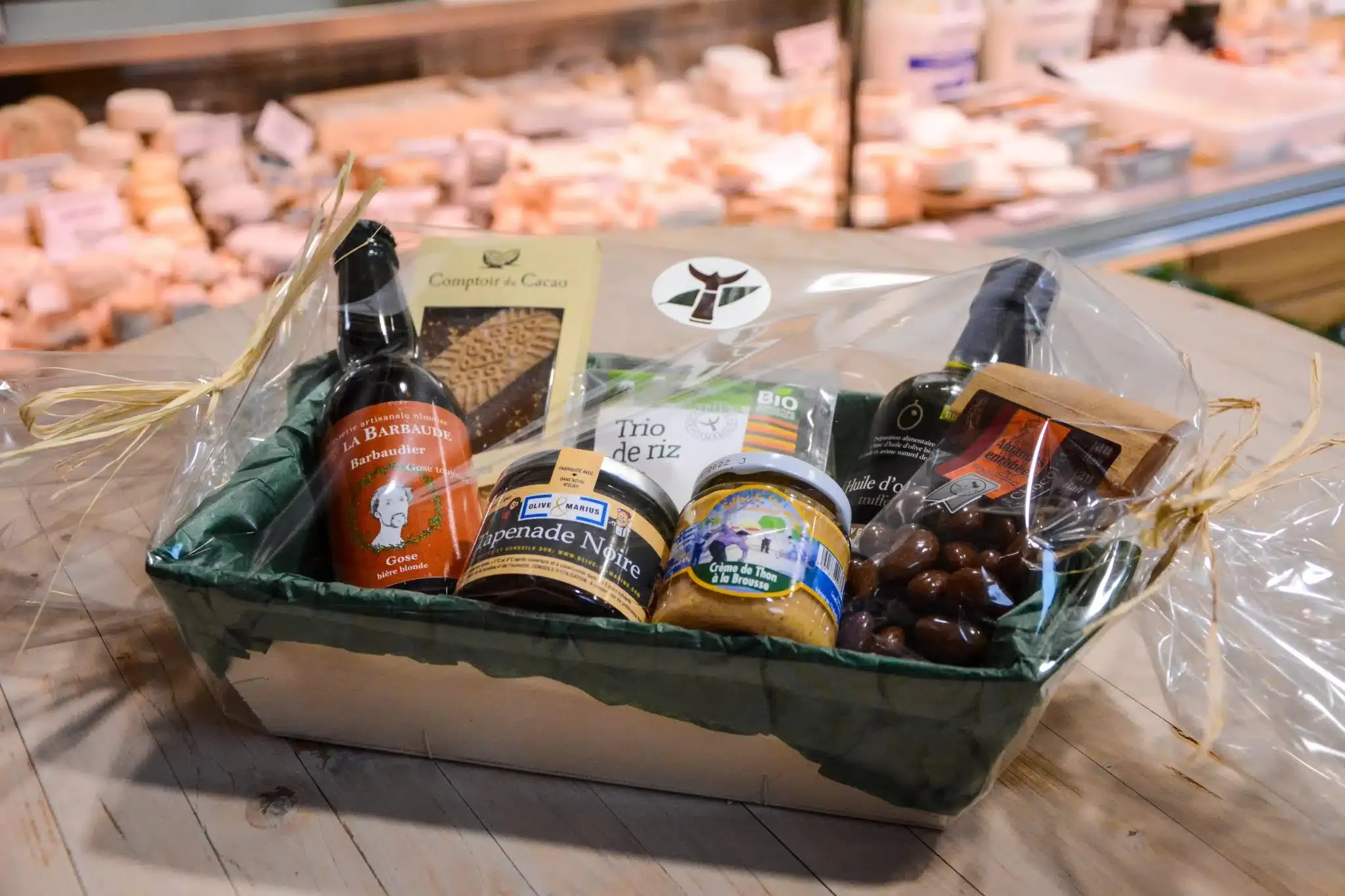 Un coffret garni de bière artisanale, tapenade, chocolats et huile d’olive, emballé sous film