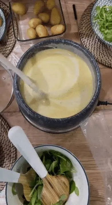 Un caquelon de fondue servi à table, entouré de pommes de terre et d’une salade