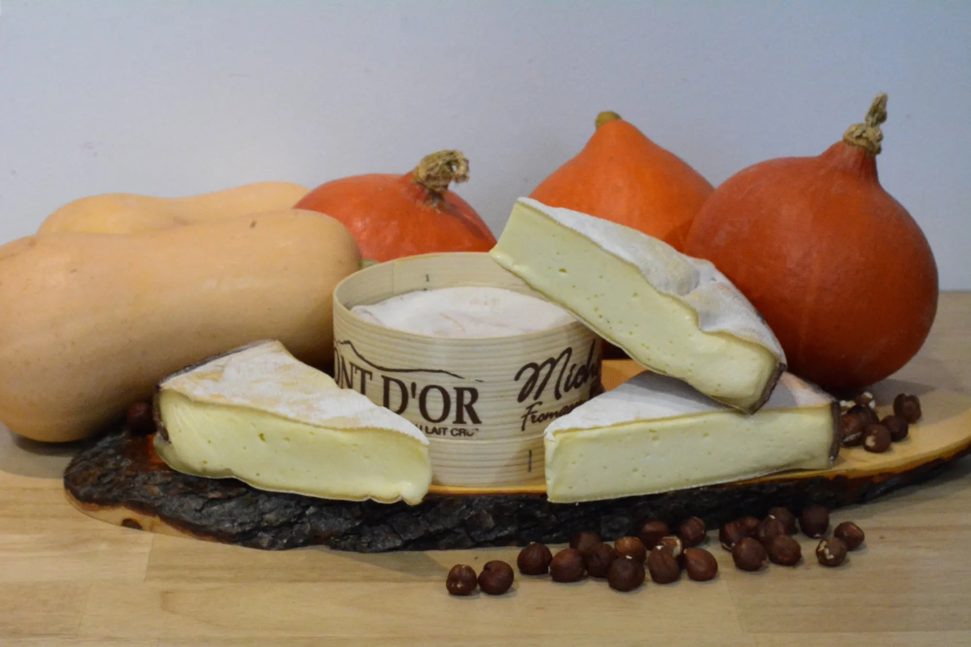 Un Vacherin Mont-d’Or dans sa boîte d’épicéa, entouré de courges et de noisettes