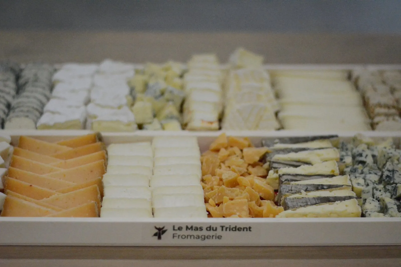 Un plateau de fromages composé en caisse de bois, rangé en bandes régulières : pâtes pressées, chèvres, morbier et bleu.