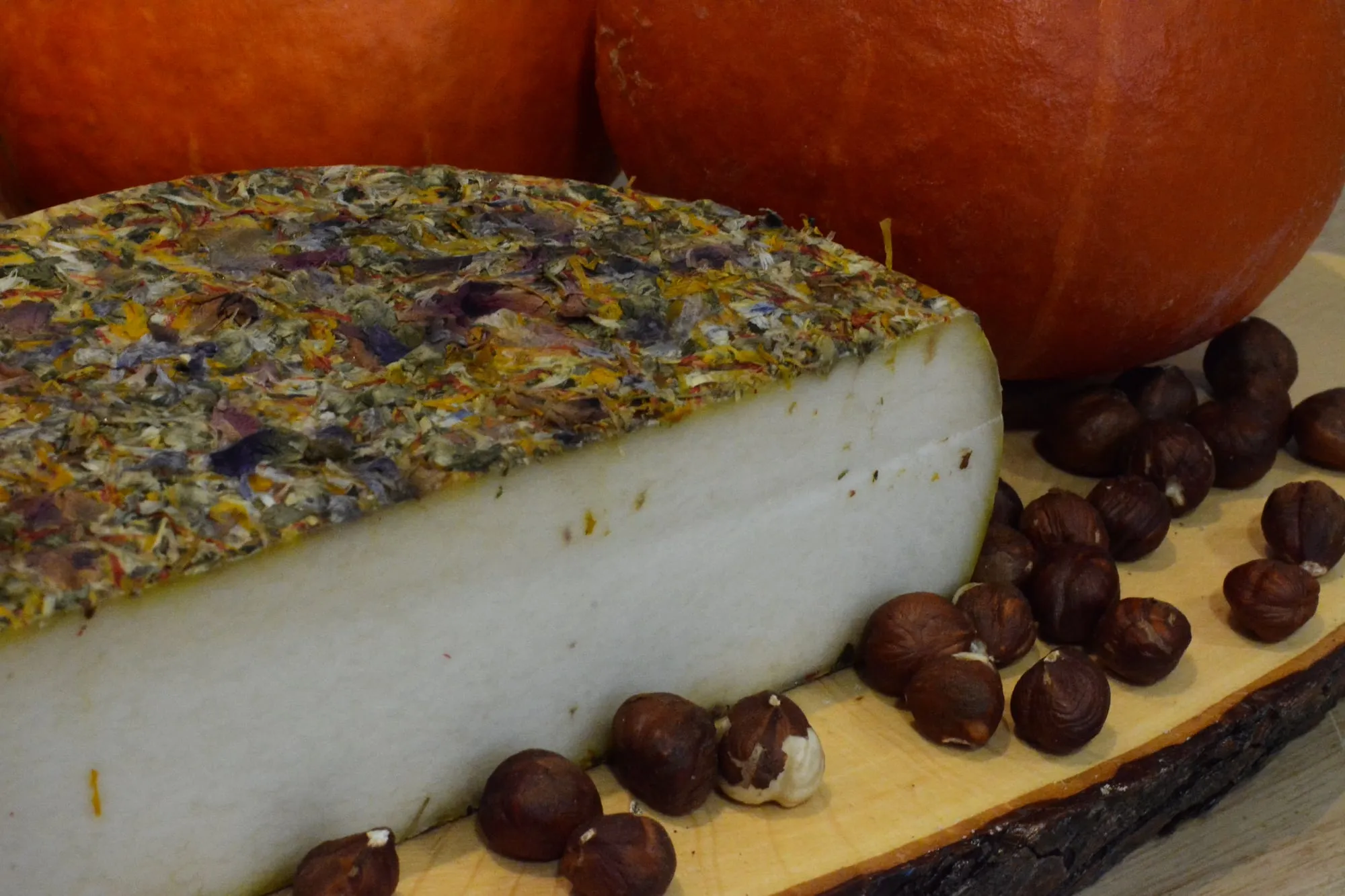 Une tomme affinée recouverte de fleurs comestibles, coupée en deux sur une planche