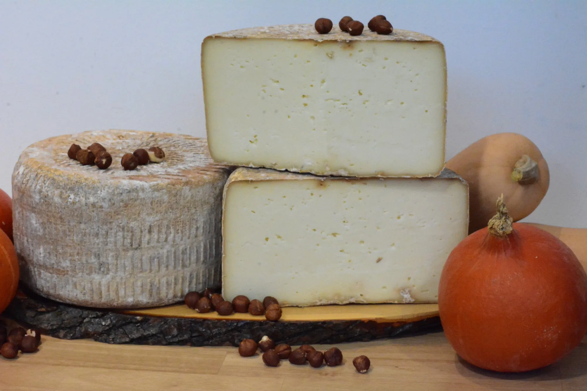 Une tomme fermière au lait cru, coupée, présentée sur une planche avec des courges